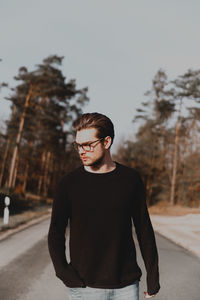 Young man standing by tree against sky