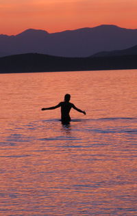 Silhouette person in sea against sky during sunset