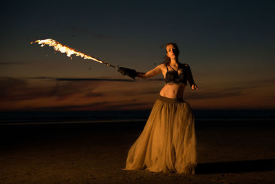 Woman standing at beach against sky during sunset