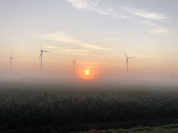 Wind turbines on field against sky during sunset