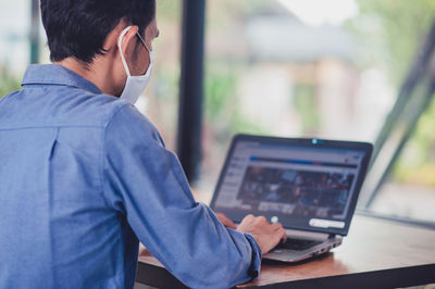 Man wearing mask using laptop at desk