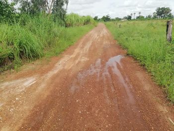 Dirt road amidst field against sky