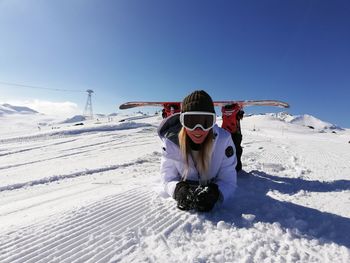 Woman with board lying on snow against clear sky