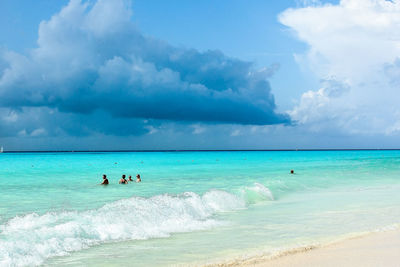 People swimming in sea against cloudy sky