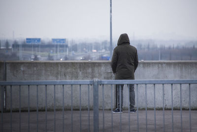 Rear view of man on railing by river in city