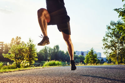 Low section of man running on road against trees