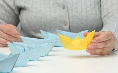 Group of blue paper boats follows a yellow boat in front of a white table. the concept of a stron