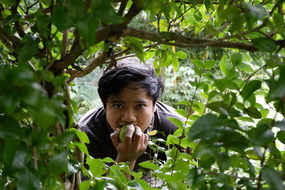 Portrait of young man eating fruit while standing by tree