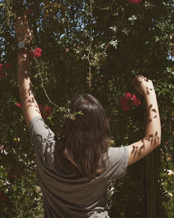 Rear view of woman holding flowering plants against trees