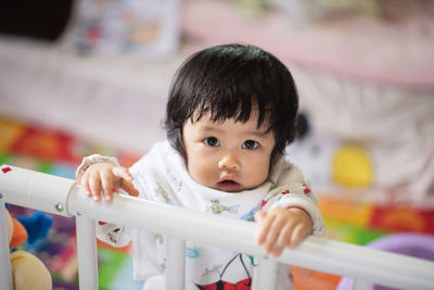 Portrait of cute girl by railing in crib