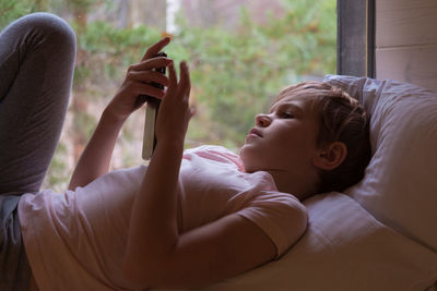 Young woman using mobile phone while lying on bed at home