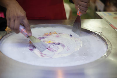 Midsection of man making ice cream rolls in kitchen