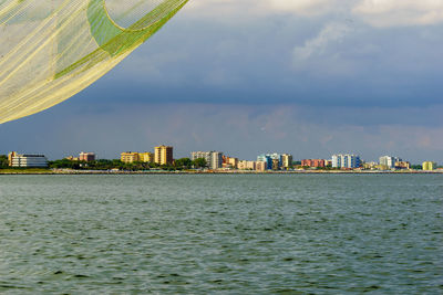 Sea by buildings in city against sky