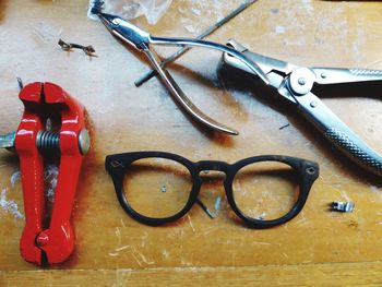 High angle view of damaged eyeglasses by pliers on table in workshop