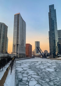 Snow covered buildings against sky during sunset