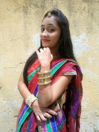 Portrait of young woman in sari standing against wall