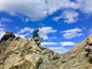Low angle view of man sitting on rocky mountains against sky