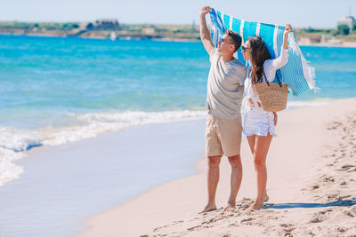 Full length of couple holding scarf standing on beach