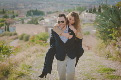 Man giving piggy back ride to happy woman standing on land