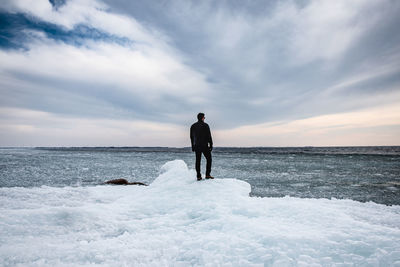 Man standing on an icy shoreline of a lake looking into the distance.