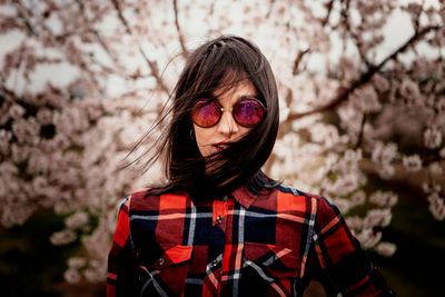 Portrait of woman wearing sunglasses against pink flowers