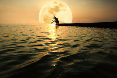 Silhouette man sailing boat in sea against moon during sunset