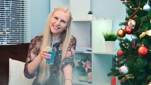 Portrait of young woman standing by christmas tree