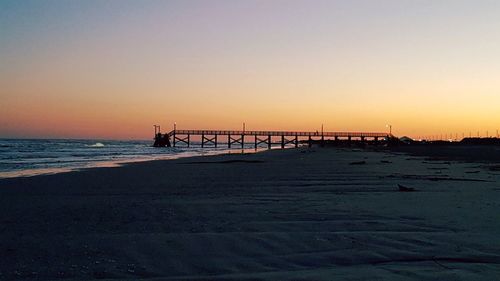 Pier at beach against clear sky at dusk