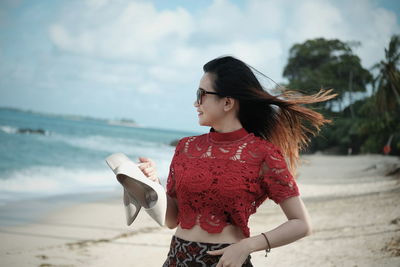 Young woman holding umbrella at beach against sky
