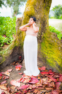 Young woman standing by tree trunk