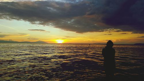 Silhouette of man on beach against dramatic sky