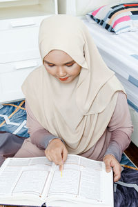 Young woman reading book while sitting on bed