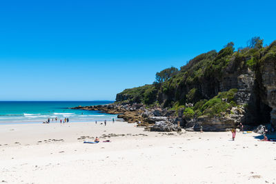 People on beach against clear blue sky