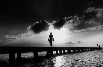 Silhouette of man standing on pier at sea against sky