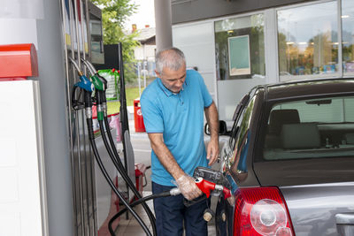 Mature man pouring petrol into tank of his vehicle on filling station. travel,transportation 