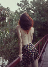 Rear view of shirtless woman standing on bridge against trees