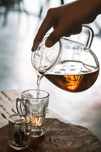 Close-up of hand pouring tea in glass on table