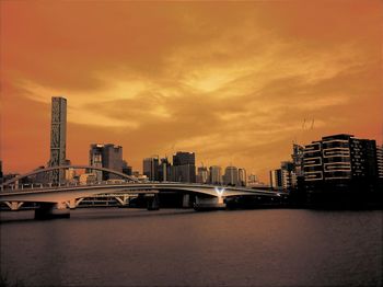 Bridge over river in city against cloudy sky