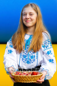 Ukrainian girl in vyshyvanka holding basket of colored red eggs on ukrainian flag background. easter