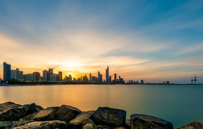Sea by city buildings against sky during sunset