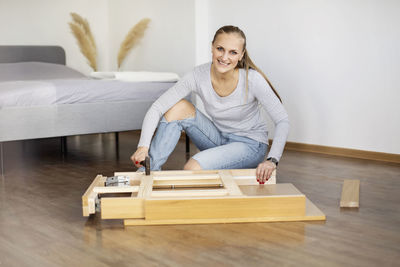 Happy woman collects furniture with a hammer in the bedroom