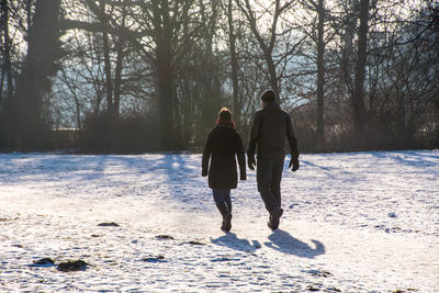 Rear view of friends walking on snow covered field in forest