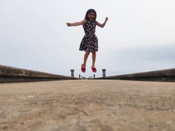 Full length of a girl jumping against sky