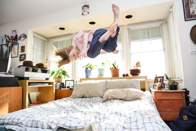 Teenager jumping on bed caught mid air and smiling in sunny bedroom