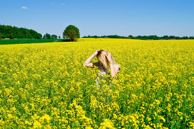 Woman standing amidst yellow flowering field against clear sky