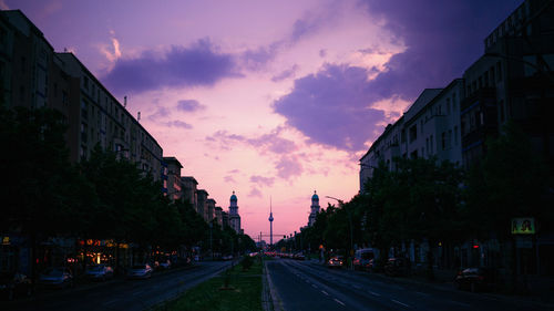 Road amidst buildings against sky during sunset