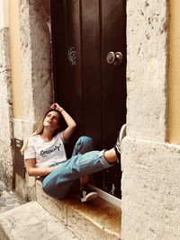 Full length of young woman sitting on door