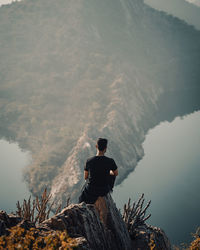 Rear view of man sitting on cliff