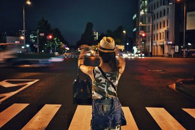 Rear view of woman photographing on city street at night