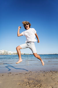 Woman jumping on beach against clear blue sky